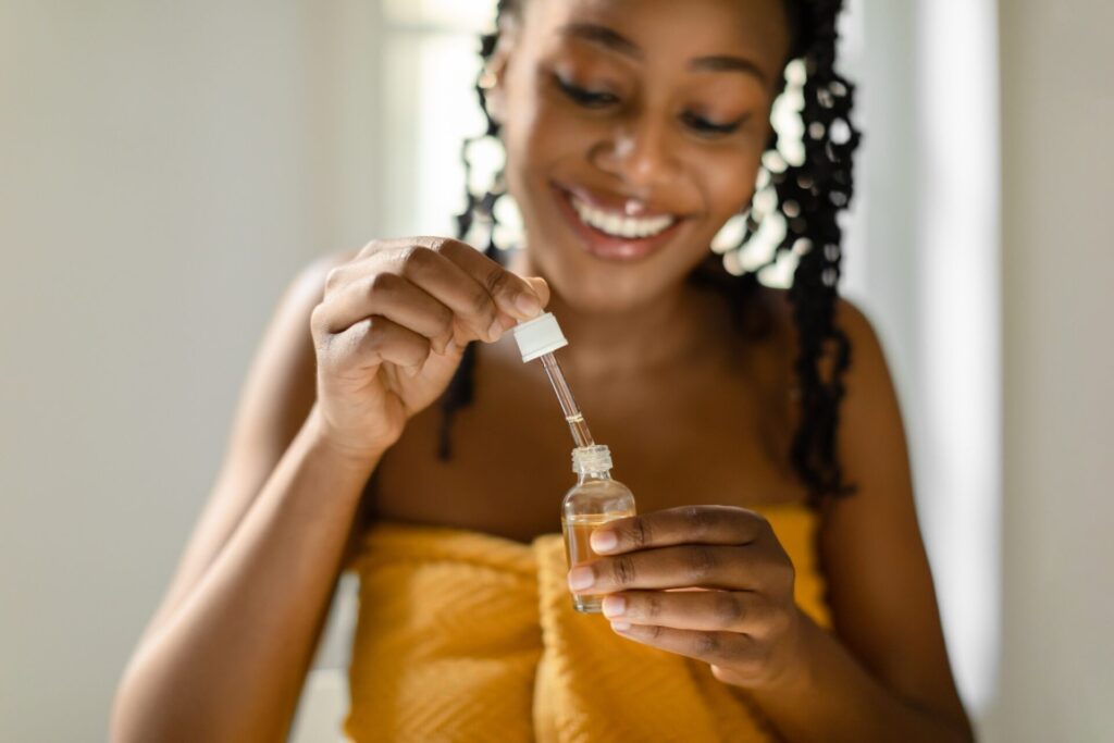 black lady holding open bottle with moisturizing face serum enjoying making daily skin care.jpg